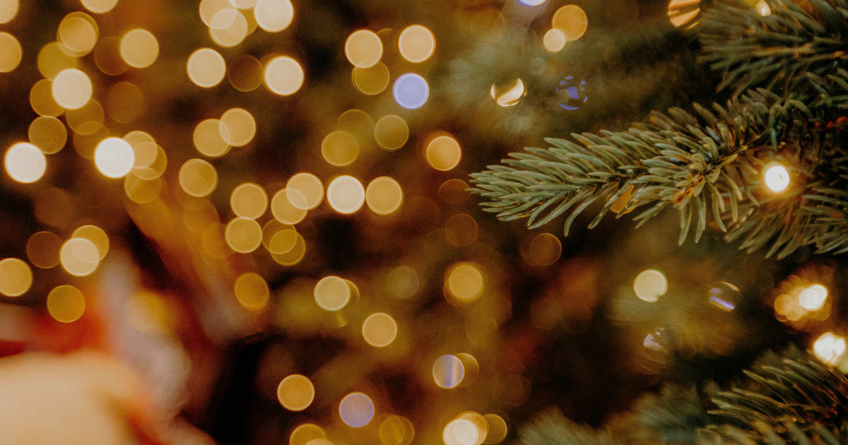 Warm holiday bokeh lights and evergreen branch background representing mindful year-end planning and financial balance.