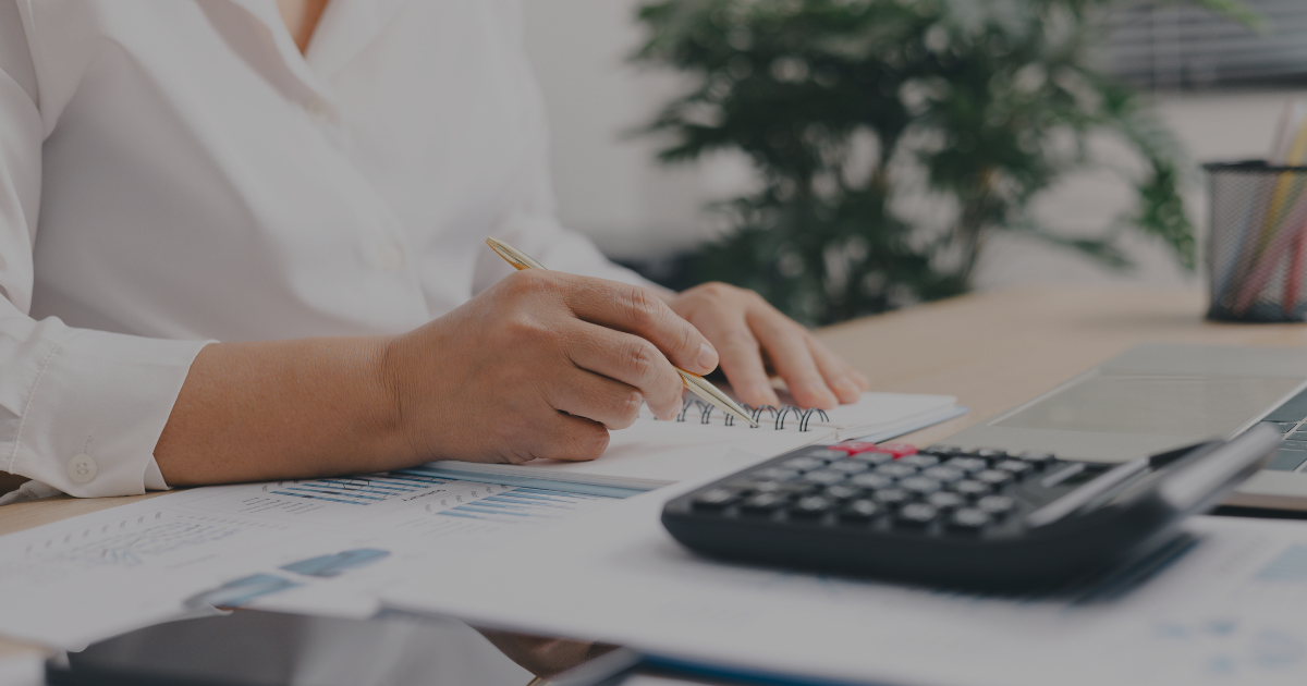 Person preparing for tax season by reviewing financial documents and writing notes beside a calculator and laptop.