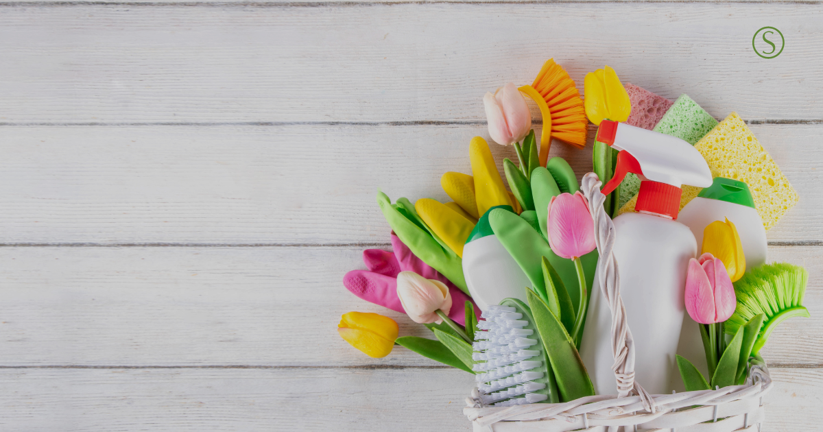 Spring cleaning supplies in a basket with flowers on a light background