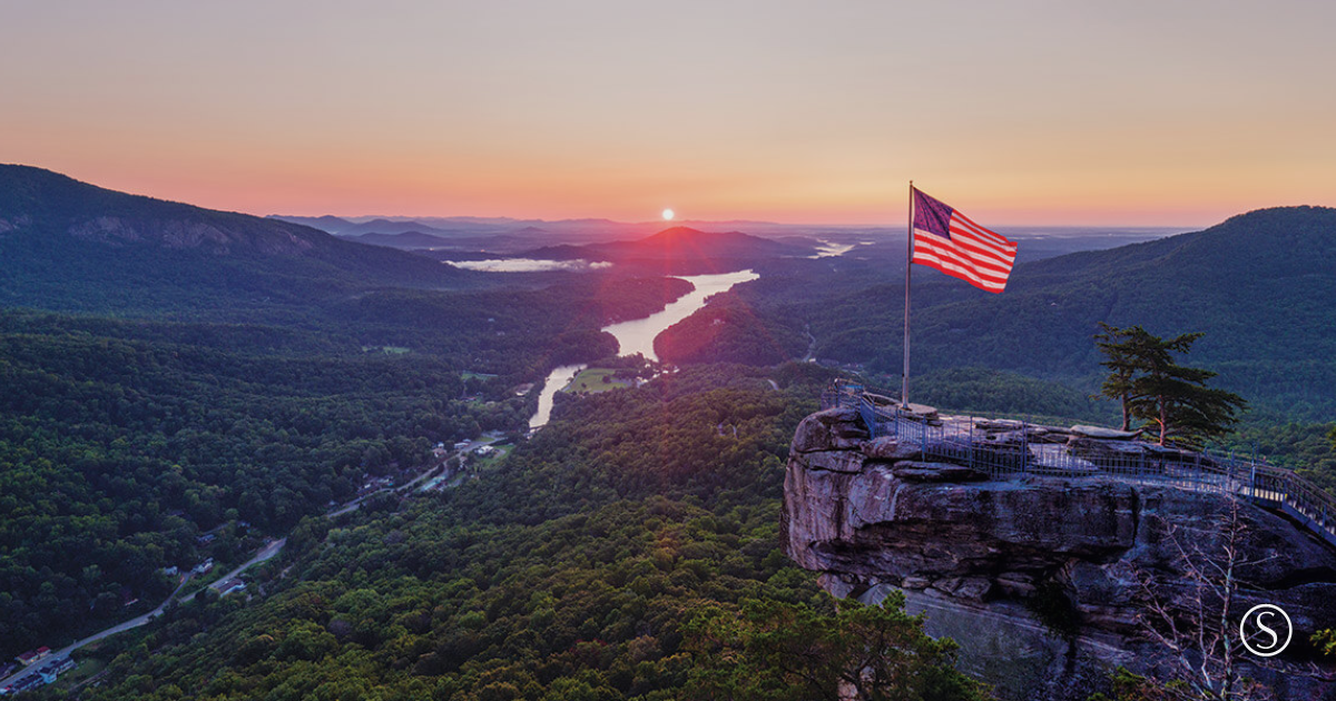 American flag overlooking the Blue Ridge Mountains at Chimney Rock during sunrise, symbolizing resilience and a long-term perspective.
